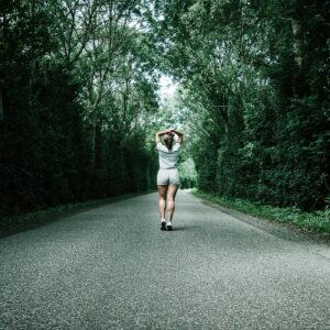 A woman jogs down a tree-lined road, embodying fitness and nature in a serene summer setting.